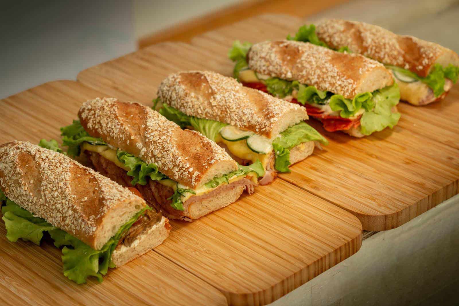 Homemade Sandwichery deli sandwiches on toasted seeded rolls with fresh lettuce, served on a wooden board